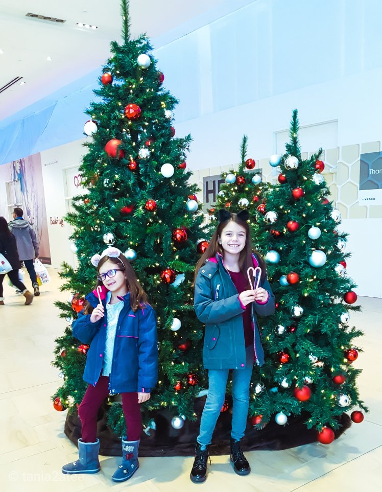 Sisters standing with candy canes in front of decorated Christmas Trees: tania2atee