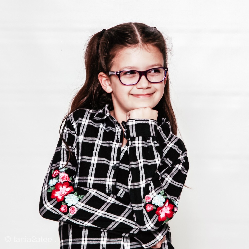 little girl wearing glasses and posing with her hand under her chin