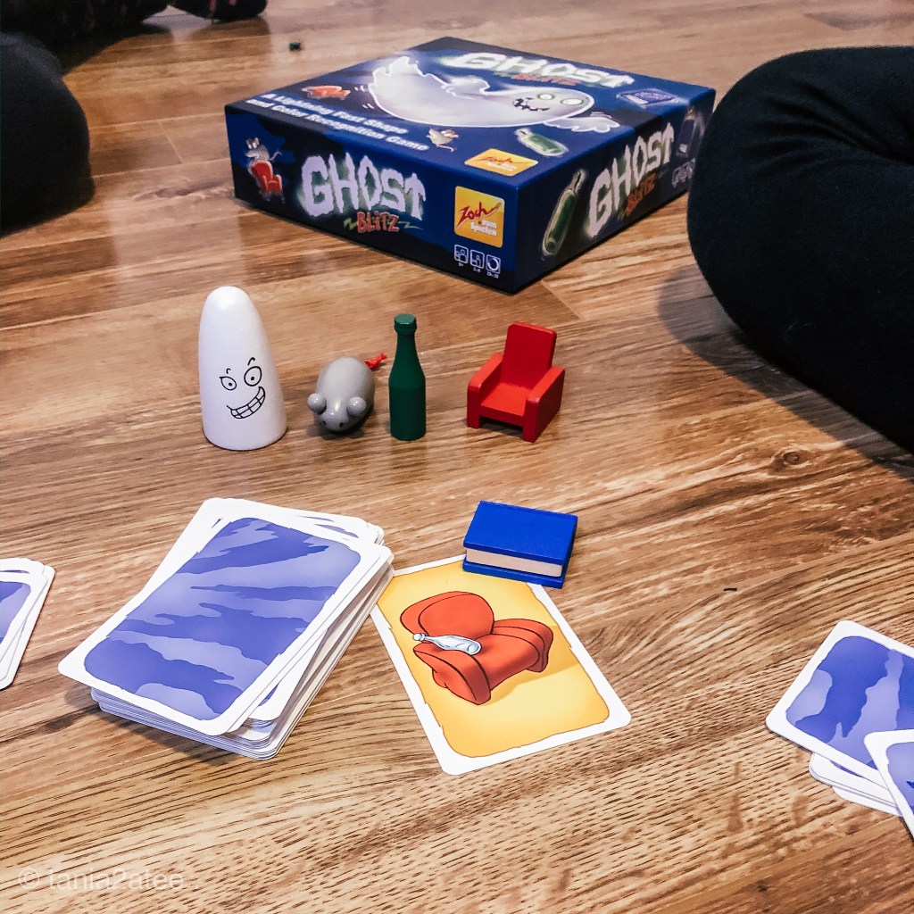 close-up of game pieces including cards and minature red chair, green bottle, grey mouse, white ghost and blue book. 