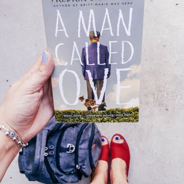 holding book and looking down at bag and shoes
